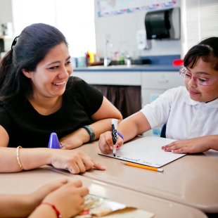 A teaching smiling at a student writing on a white board at a desk
