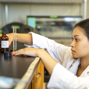 A student in a lab is eye level with the table, looking at a sample she just poured