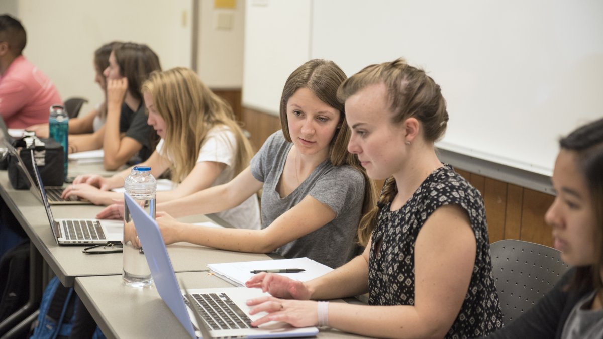 2 students in class looking at one laptop screen