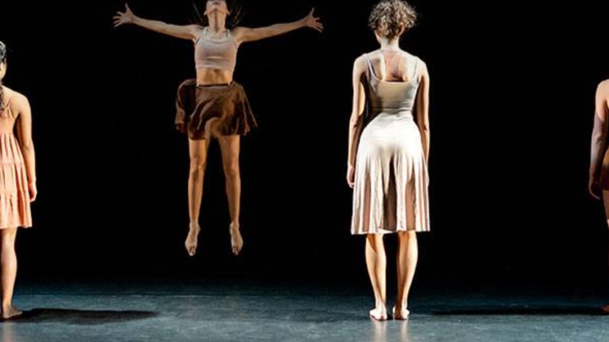 A group of dancers with their backs to the audience while the middle dancer jumps