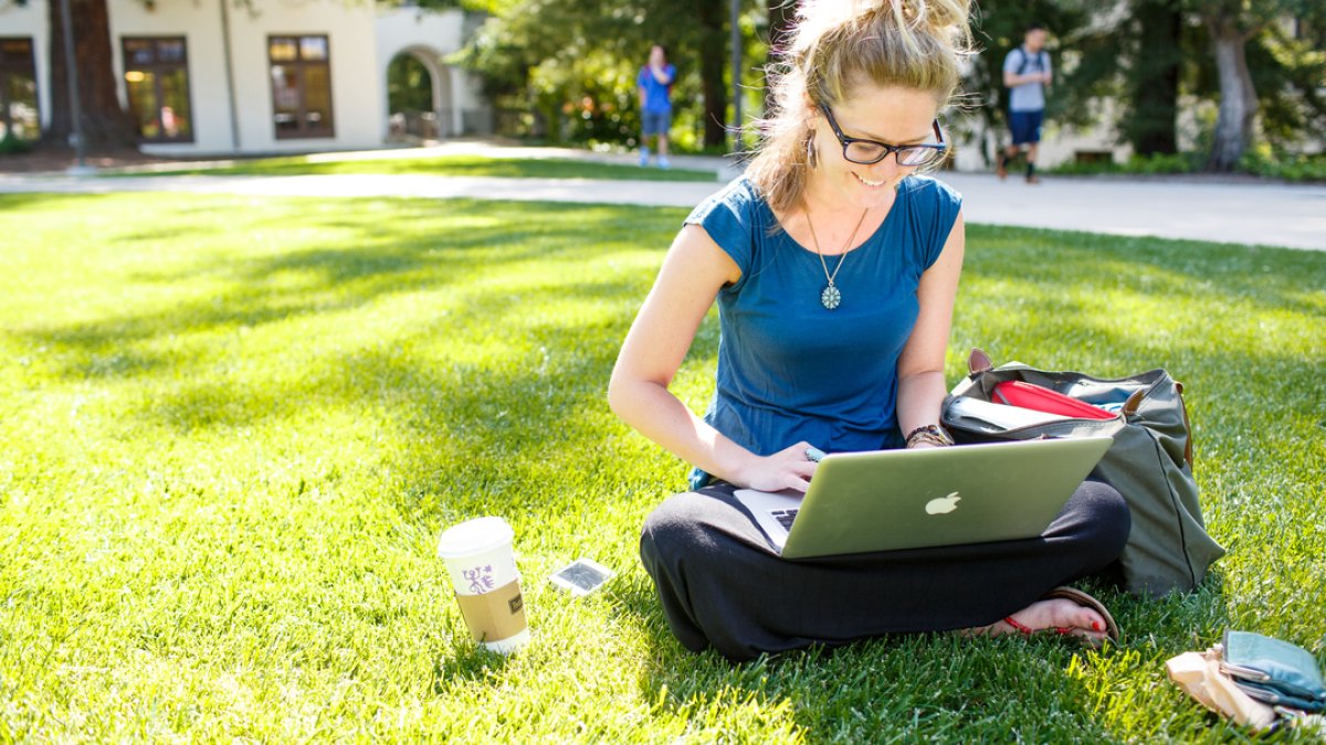 A student sitting on the lawn studying with her laptop 