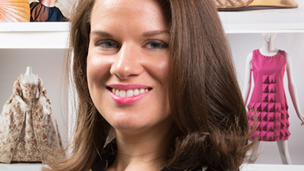 woman standing at an angle in-front of images of fashion smiling 