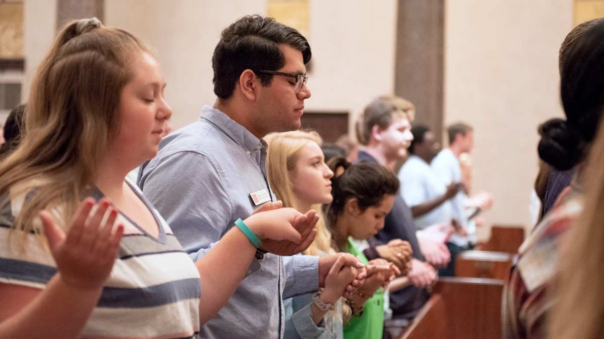 Students holding hands praying during mass