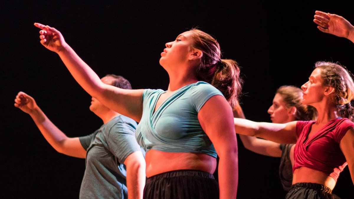 Five graduate Dance students pointing upwards in front of a black curtain.