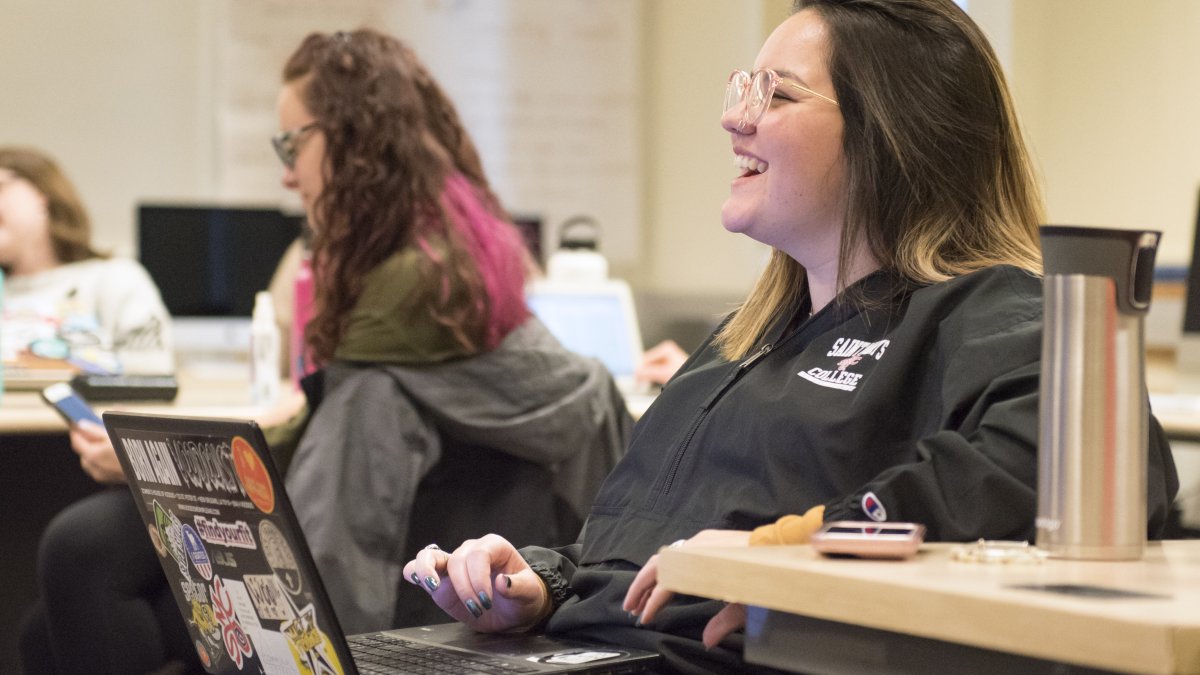 Woman laughs while using her computer in a classroom
