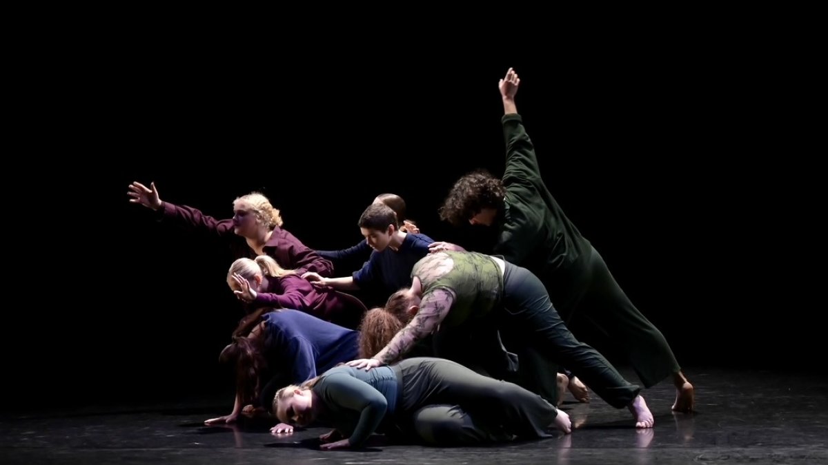 A group of dancers grouped in a dramatic way with a black background and light shining on them.