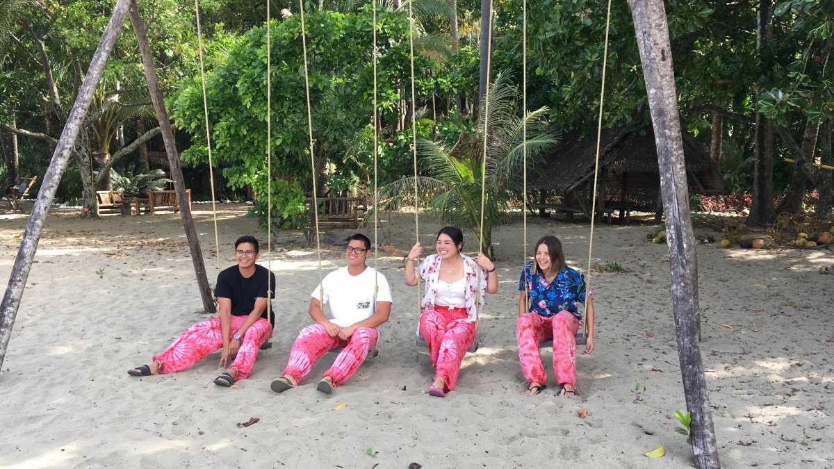 Students hanging on swings in the sand
