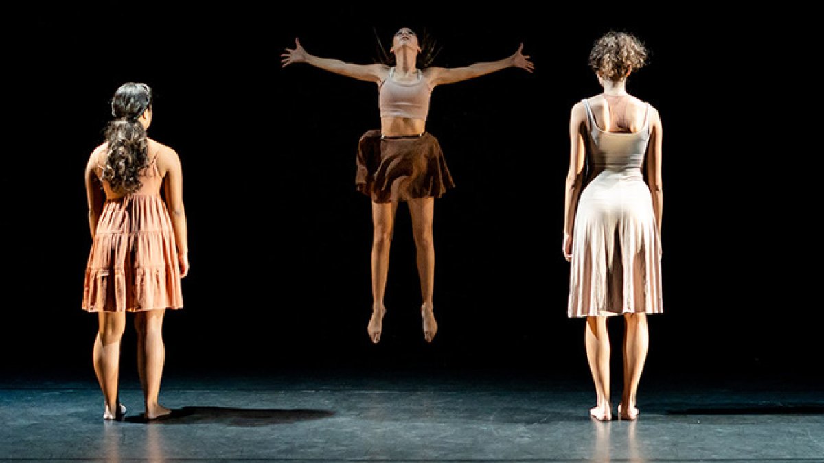 A group of dancers with their backs to the audience while the middle dancer jumps