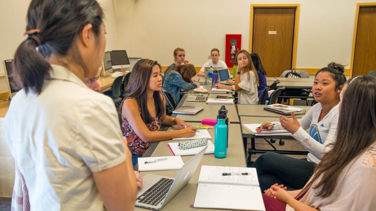 girl standing and talking in front of many students in a classroom